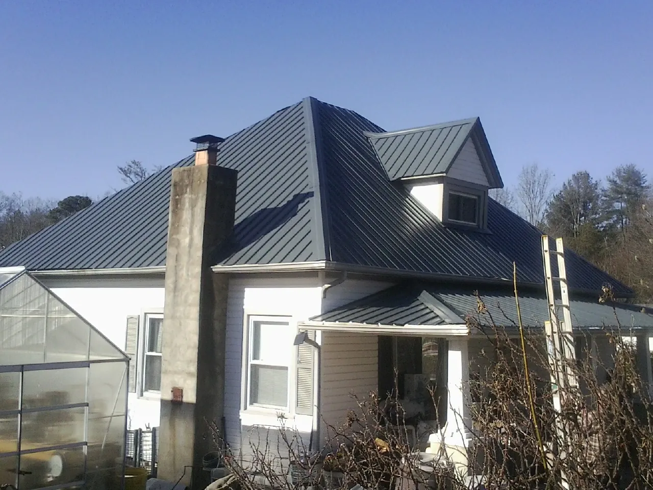 Dark blue standing seam metal roof on a white farmhouse with dormer — Slate & Tile Roof Repair by Roofing Brothers in West Elkton