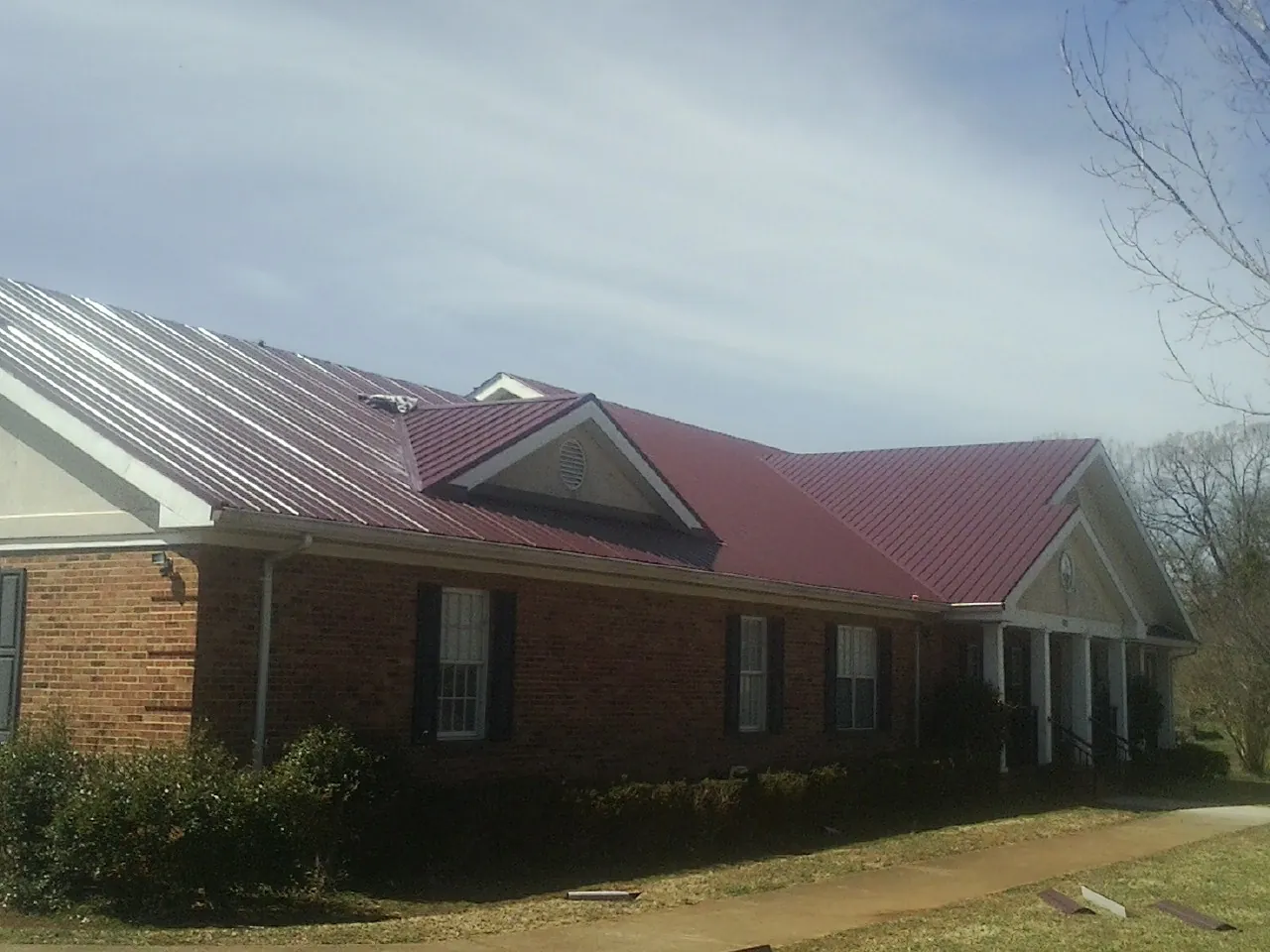 Red metal roof with gabled entries on a long brick building, from a Hail Damage Roof Repair job in West Elkton