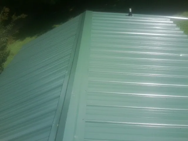 New green metal panels meeting at the ridge of a roof — Flat Roof Repair work by our crew in West Elkton