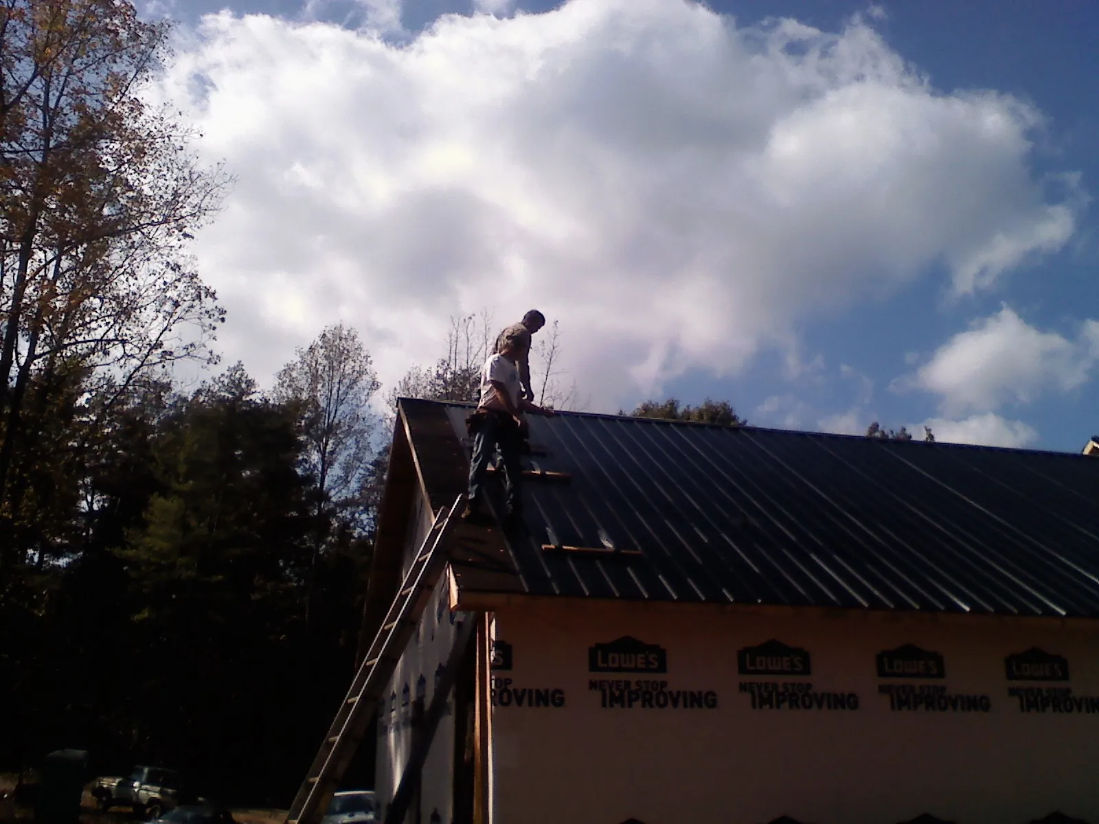 Roofer fastening dark metal panels high against a cloudy sky, from a Roof Inspection job in West Elkton
