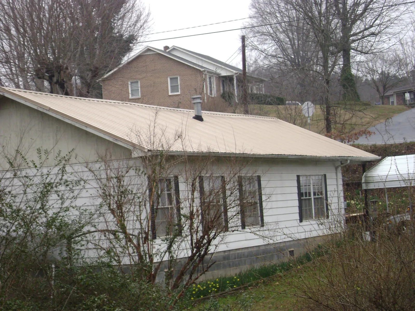 Tan metal roof on a white sided house set into a hillside — Commercial Roofing by Roofing Brothers in West Elkton